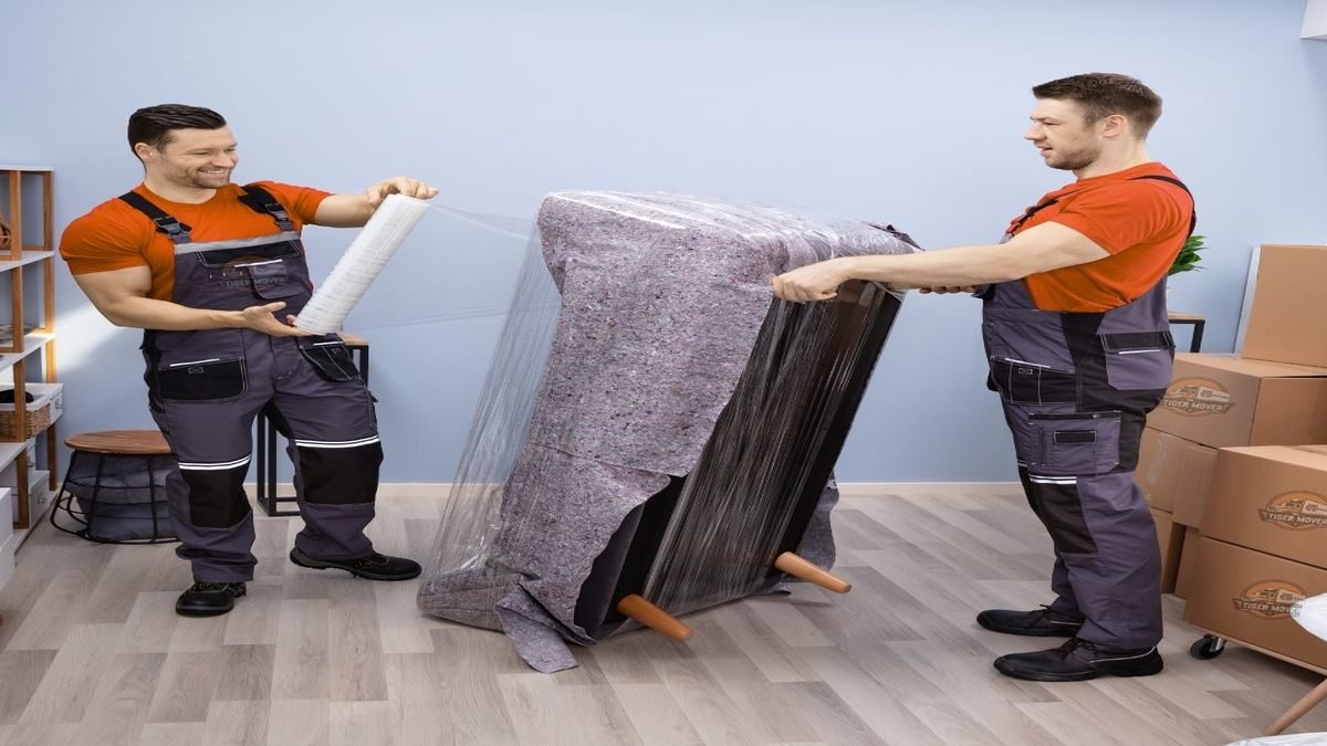 Two movers packing household items using bubble wrap and boxes