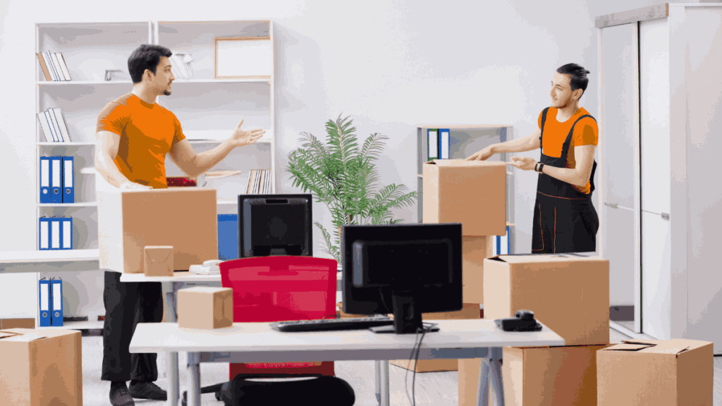 Professional movers handling office desks, chairs, and IT equipment in a corporate environment